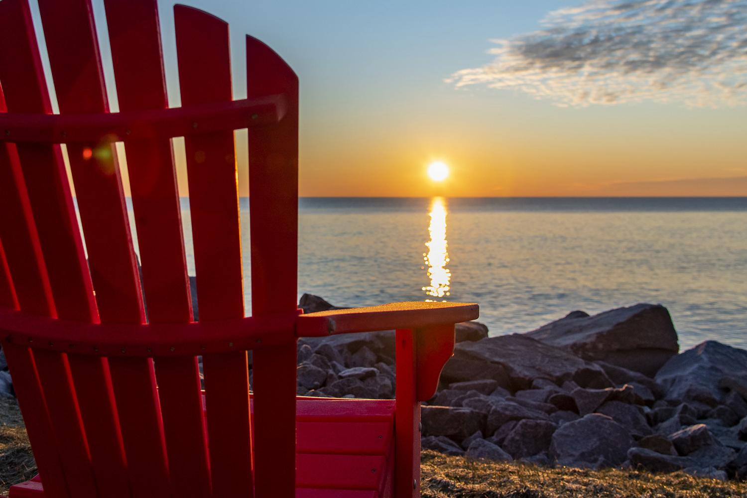 A red Adirondack chair facing the lake at sunrise.